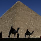 People, including two men on camels, are silhouetted against the Great Pyramid in Giza.