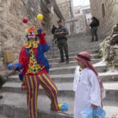 Five Israeli soldiers stand around two Jewish settlers dressed in costumes.