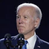 Joe Biden gives a speech into two microphones, with two American flags in the background.
