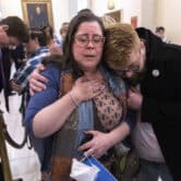 A person hugs Christine Cox as she puts her hand on her chest in a hallway outside the Georgia state Senate.