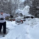 A man shovels snow from his driveway and sidewalk.