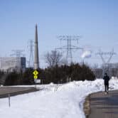 People walk on a trail with snow on the ground around them and a nuclear power plant in the background.