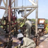 Two Chadians guide a pipe down an oil well.