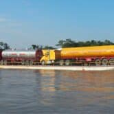 Several trucks with tankers in the back stand on a platform sailing through the river.