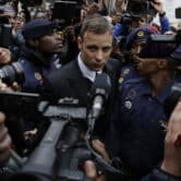 Police officers and members of the media surround Oscar Pistorius as he leaves court.