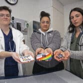 Three West Virginia University students hold materials related to the LGBTQA community.