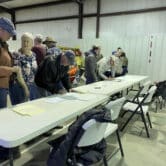 People stand in front of a plastic folding table in a barn to sign documents.