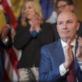 Several people stand behind Spencer Cox as he applauds during a ceremony at the Capitol building in Salt Lake City.