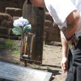 A man looks over the gravesite marked with a blue flower and a marker reading "Sacred to the Memory of Antonio Garra Sr. A Leader Among Hi People. Cupeno-Kavalim Clan. Died January 10. 1852"