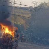 Two people stand next to a burning tractor.