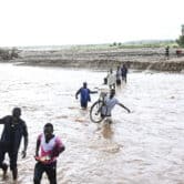 Nine people carry various objects as they wade through floodwaters in Malawi.