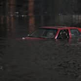 An empty red car with one window down is surrounded by floodwaters on a road in Oakland, California.
