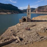 People stand near a church and the remains of an ancient village in a water reservoir in Spain.