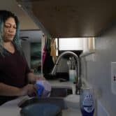 A woman cleans dishes using tap water.