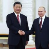 Xi Jinping and Vladimir Putin shake hands while posing for a photo.