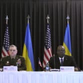 Boris Pistorius, Mark Milley, Lloyd Austin and Oleksii Reznikov sit behind a table with Ukrainian and U.S. flags in the background.