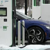 A cart is parked next to an electric vehicle charging station, with snow on the ground around it.