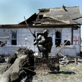 A knight statue stands in front of a house severely damaged by a tornado.