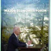Joe Biden sits at a desk next to a screen displaying a forest and the words "Major Economies Forum on Energy and Climate."