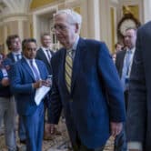 Several people look at Mitch McConnell as he walks through the U.S. Capitol.
