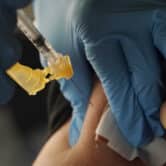 A nurse wearing blue nitrile gloves administers a Moderna Covid-19 vaccine shot.