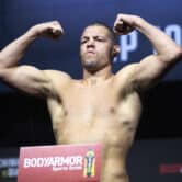 Nate Diaz flexes while standing on a scale on a stage during a ceremonial weigh-in.
