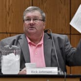 Rick Johnson holds up a white card with writing on it while sitting at a table during a meeting.