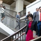 Susan Collins and half a dozen other people walk down stairs inside a building on Capitol Hill.