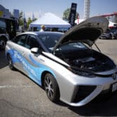 A gray 2021 Toyota Prius with its hood open and the words "powered by hydrogen fuel" displayed on the right-side doors.
