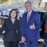 Several people surround Tsai Ing-wen and Kevin McCarthy as the walk away from a pair of black SUVs.