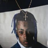 A woman wears a neckless with a cross and a t-shirt featuring a picture of XXXTentacion.