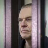 Andrzej Poczobut stands in a cage inside a Belarusian courtroom.