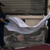 A forensic assistant and investigator put a white blanket over the body of a dead homeless man.