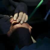 A dentist wearing gloves holds a tool while examining a patient's teeth.