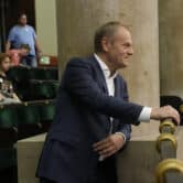 Donald Tusk rests his hand on a rail while standing in the Polish Parliament building.