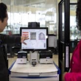 A man gestures at a computer screen showing facial recognition software at an airport, as a woman looks on.