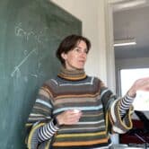 Woman in colorful sweater stands in front of blackboard