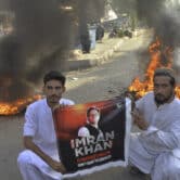 Two men hold a banner that reads "Imran Khan is Pakistan's red line, don't dare to cross it!" The banner also shows an image of Khan.
