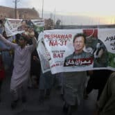 Imran Khan supporters hold two posters featuring images of the former prime minister as people gather in a street in Peshawar.