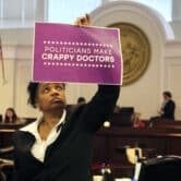 On the North Carolina Senate floor, Kandie Smith holds up a sign that reads "politicians make crappy doctors."