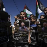 Palestinian kids wave their national flag and hold posters showing Khader Adnan during a protest.