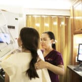 A mammographer demonstrates the mammogram process on a woman.