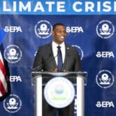 Michael Regan speaks on stage at an event, with EPA symbols and two American flags behind him.