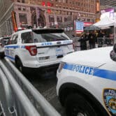 People walk by a line of NYPD vehicles.