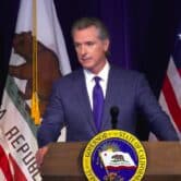 California governor Gavin Newsom wears a blue suit in front of the state flag.