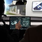 A driver clicks on a screen inside a Tesla car while a passenger looks on.