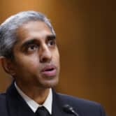 Vivek Murthy speaks into a microphone while sitting down and wearing a suit.