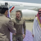 Volodymyr Zelenskyy shakes a man's hand while standing next to Prince Badr Bin Sultan at Jeddah airport.