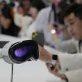 A person leans over a display table to take a photo of an Apple Vision Pro headset.