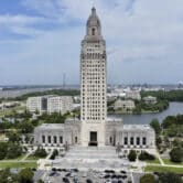 A high-up view of the Louisiana state Capitol, with buildings, tree and cars nearby.